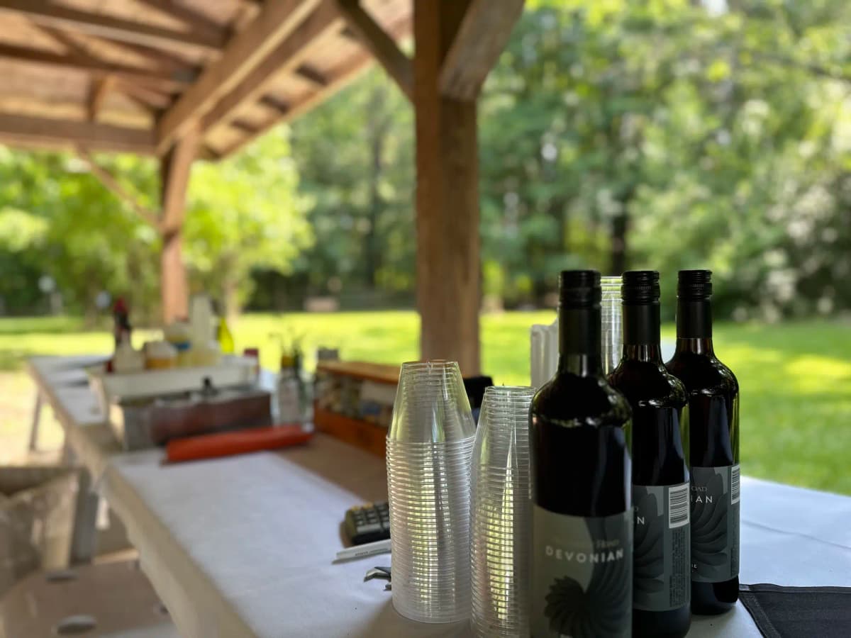 Outdoor catering setup with wine bottles and clear plastic cups