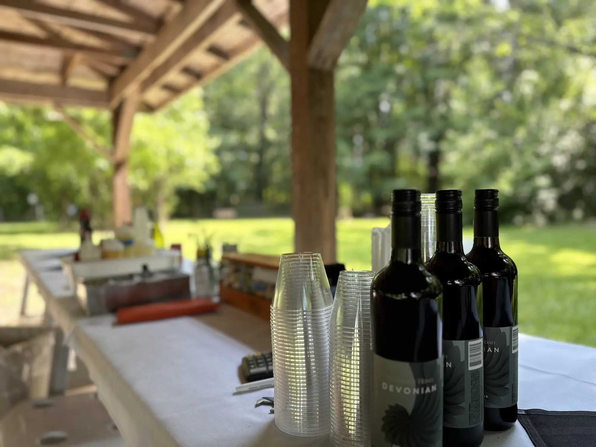 Outdoor catering setup with wine bottles and clear plastic cups