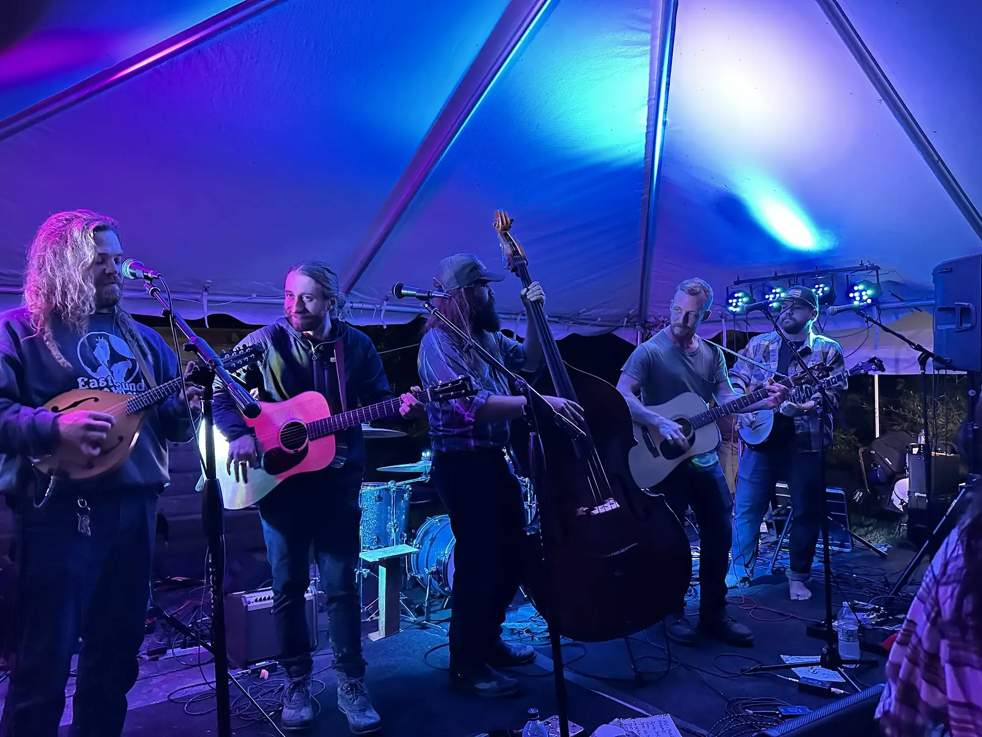 Five-piece bluegrass band with mandolin, guitars and upright bass under a blue-lit tent