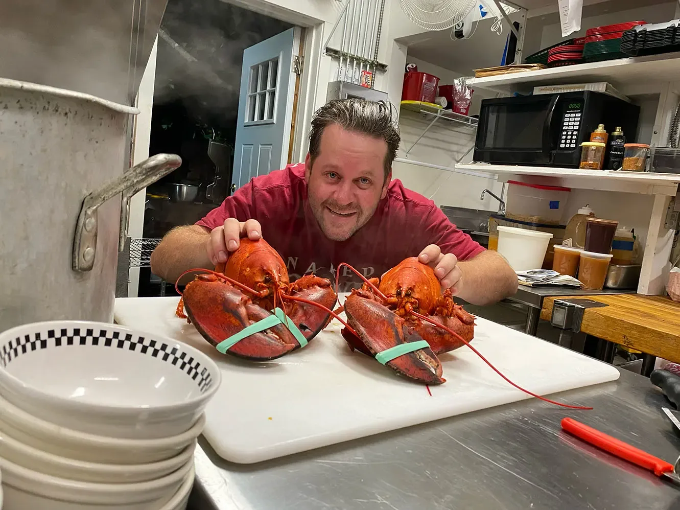 Grinning cook showing off two cooked lobsters in the kitchen