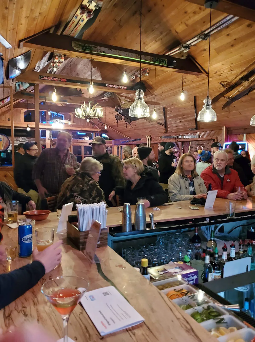 Crowded bar under a vaulted pine ceiling hung with vintage skis and an antler chandelier