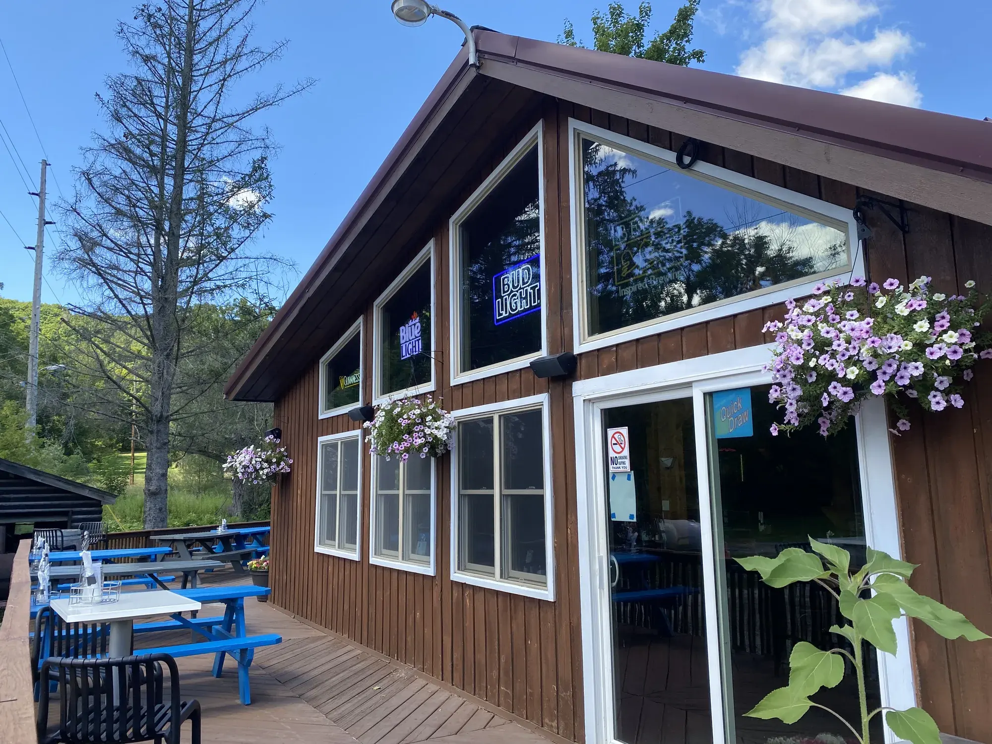 Deck with blue picnic tables beside the A-frame bar, hanging purple petunias