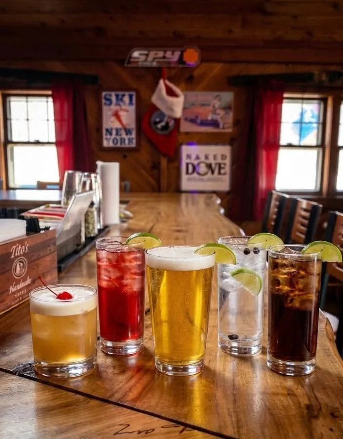 Five drinks lined up on a long wooden bar, paneled walls and ski posters behind