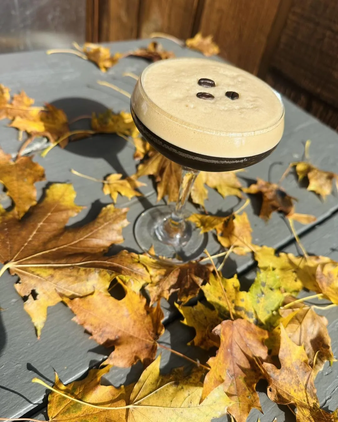 Espresso martini with coffee beans on a table scattered with autumn maple leaves
