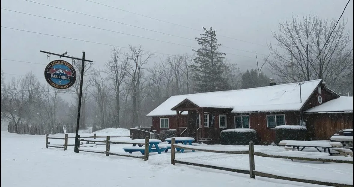 Lock Stock Bar & Grill under heavy snow with its hanging sign, picnic tables and fence