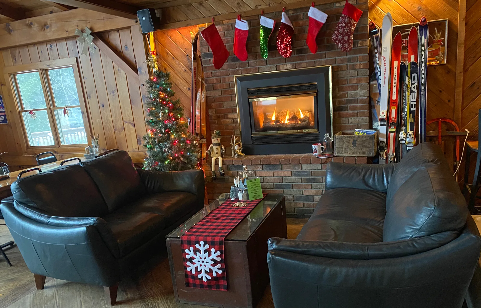 Leather sofas facing a glowing brick fireplace with stockings, Christmas tree and vintage skis