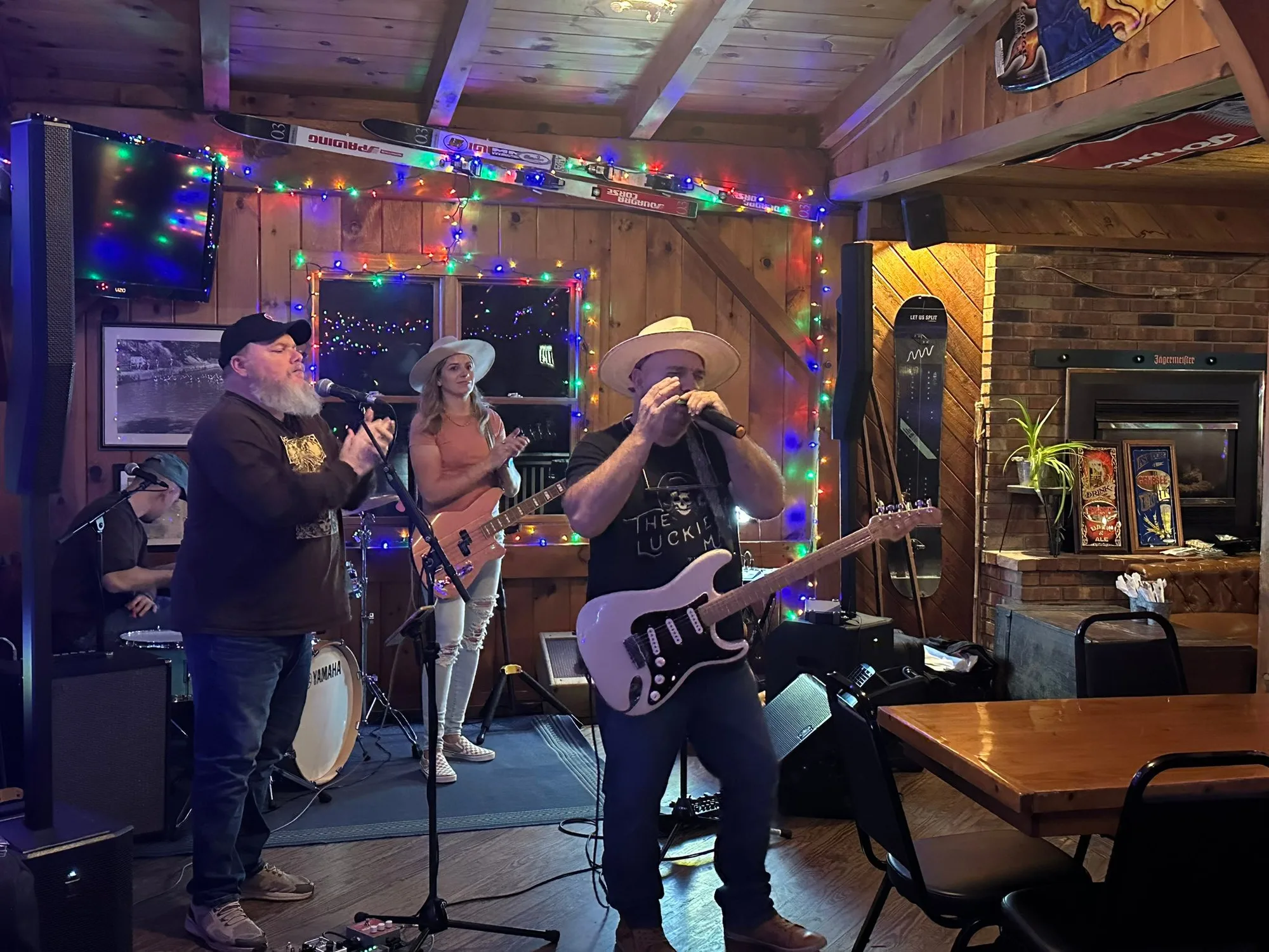 Band playing guitars and bass in a wood-paneled bar decorated with string lights