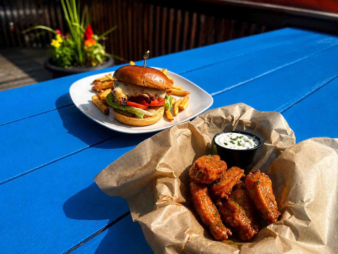 Sandwich with fries and saucy wings with ranch on a bright blue deck table